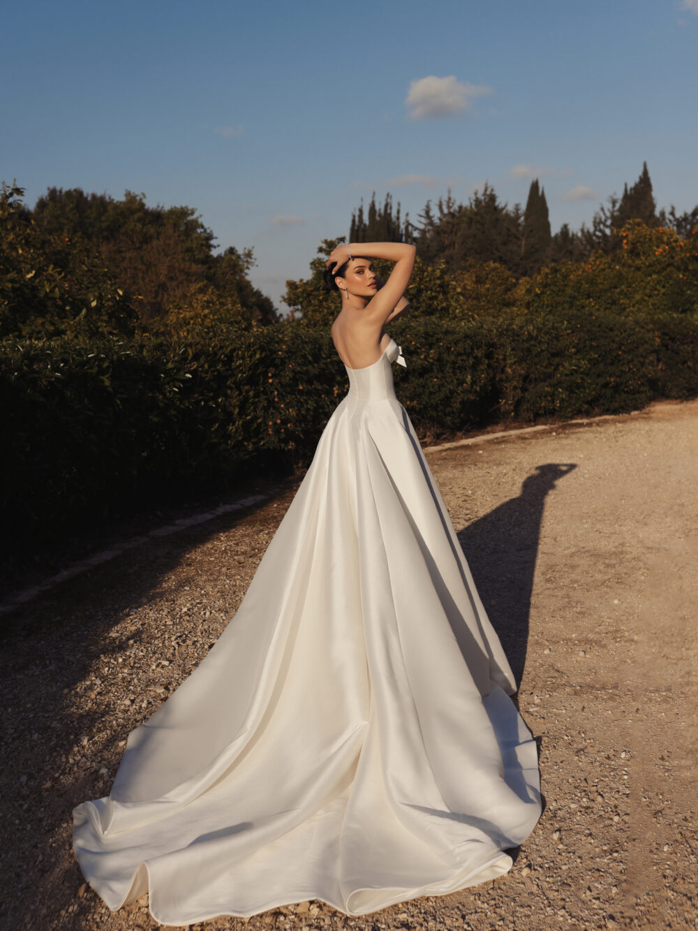 A woman poses outdoors in a strapless white ball gown with a fitted bodice and long flowing train.