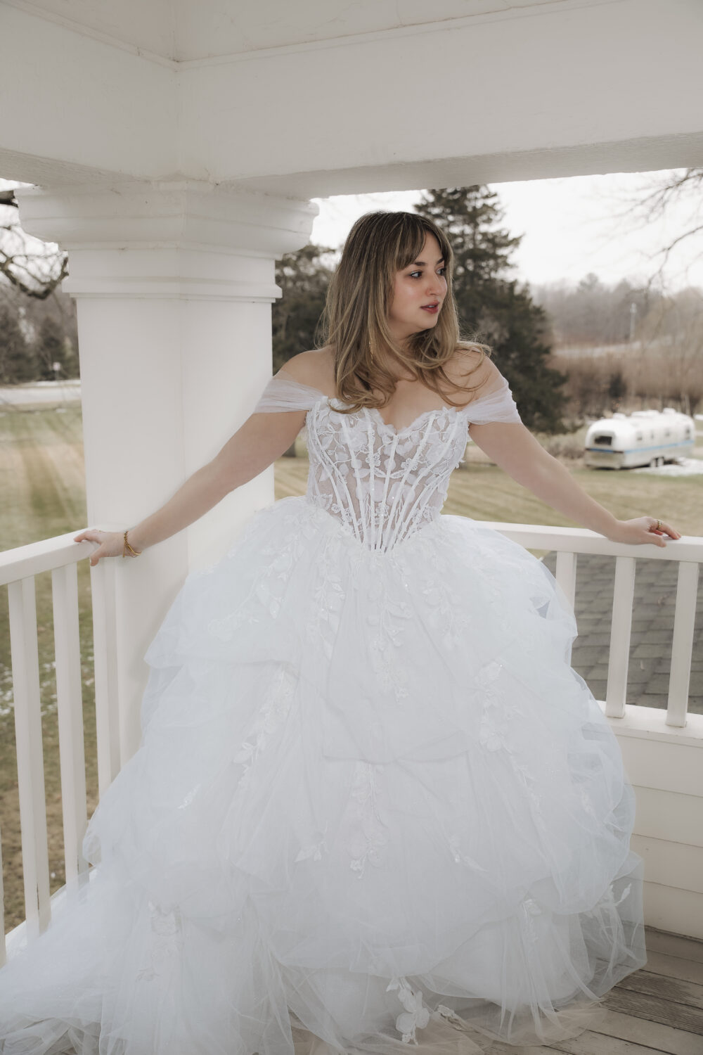 Bride posing in a bridal boutique wearing a lace wedding gown with thin straps and a flowing layered tulle skirt.