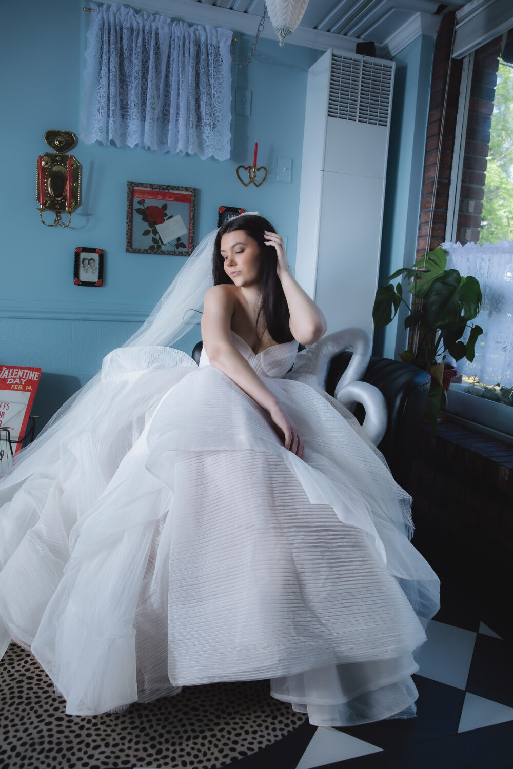 Bride seated beside a leafy tree wearing an off-the-shoulder wedding gown with sheer sleeves and a full layered tulle skirt.