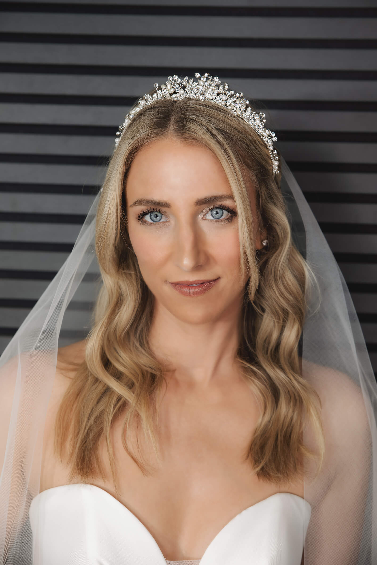 A close-up portrait shows a blonde bride wearing a pearl and crystal tiara with a sheer veil and strapless wedding gown.