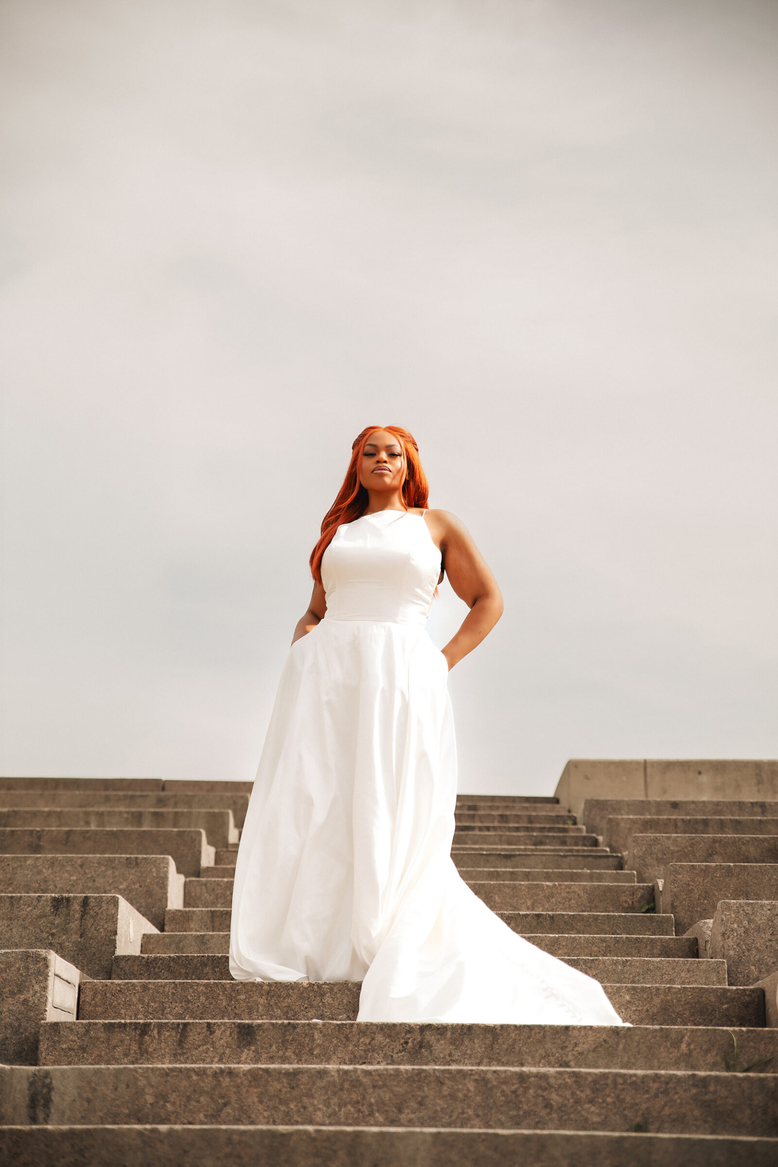 Plus-size bride in a flowing white wedding dress standing on outdoor steps.