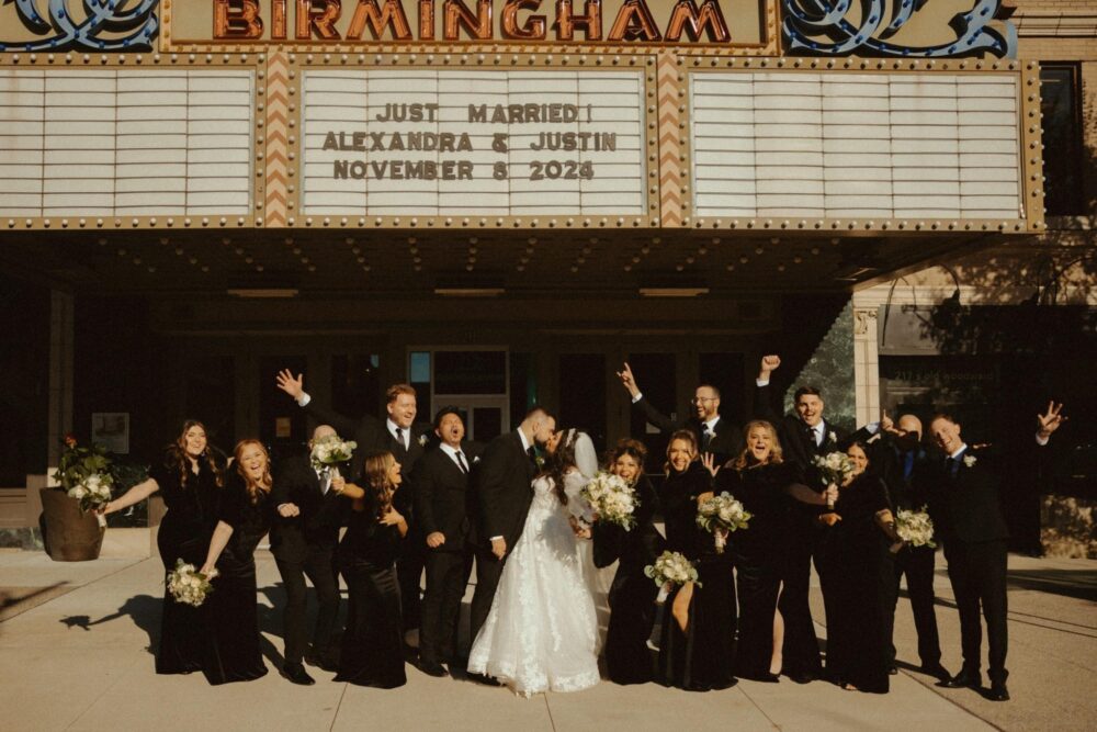 A wedding party poses beneath the Birmingham theater marquee, which reads “Just Married! Alexandra & Justin November 8, 2024.”