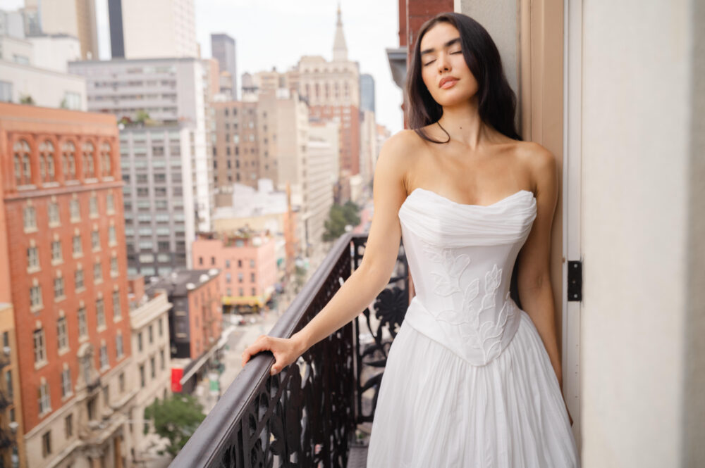 la premiere bride wearing off the shoulder wedding dress standing on a balcony