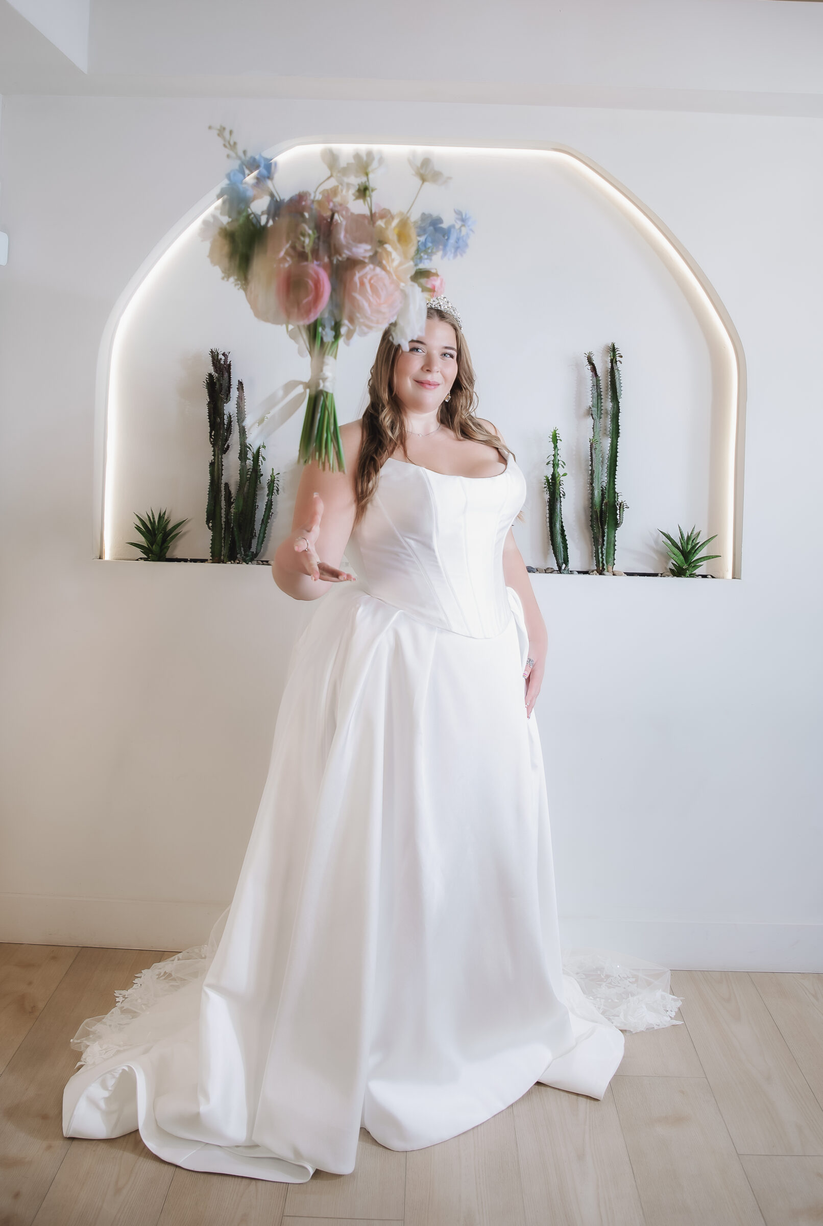 A plus-size bride in a sleeveless satin dress tosses a bouquet toward the camera.