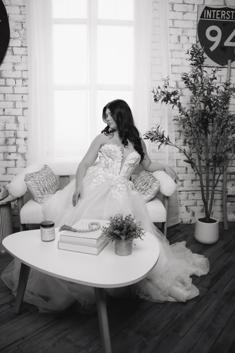Black-and-white portrait of a bride seated in a white floral wedding gown with a plunging neckline and full tulle skirt.