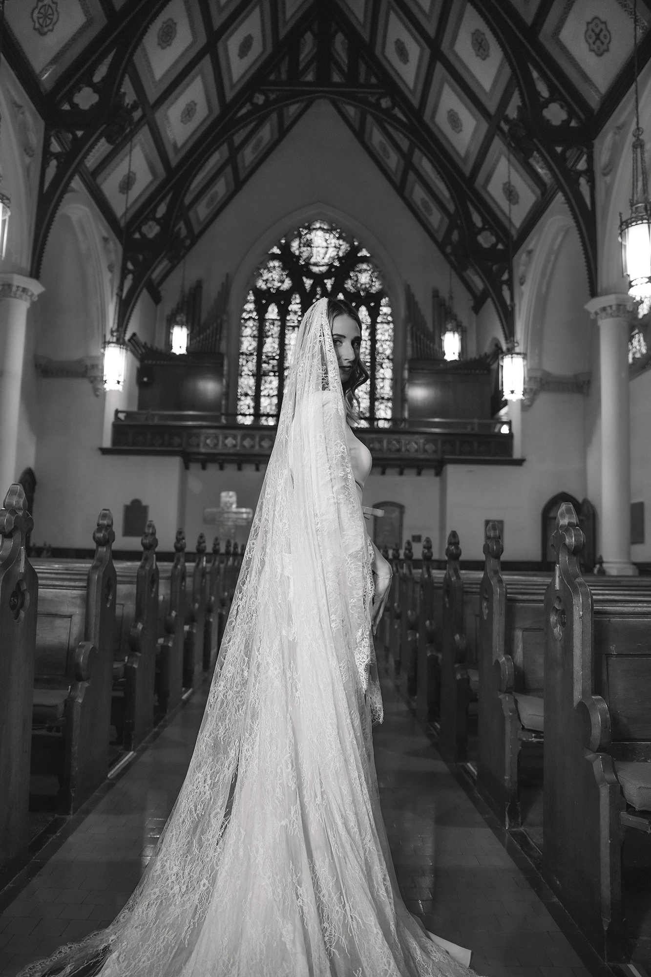 Bride in a long wedding gown and veil standing inside a Gothic-style church.