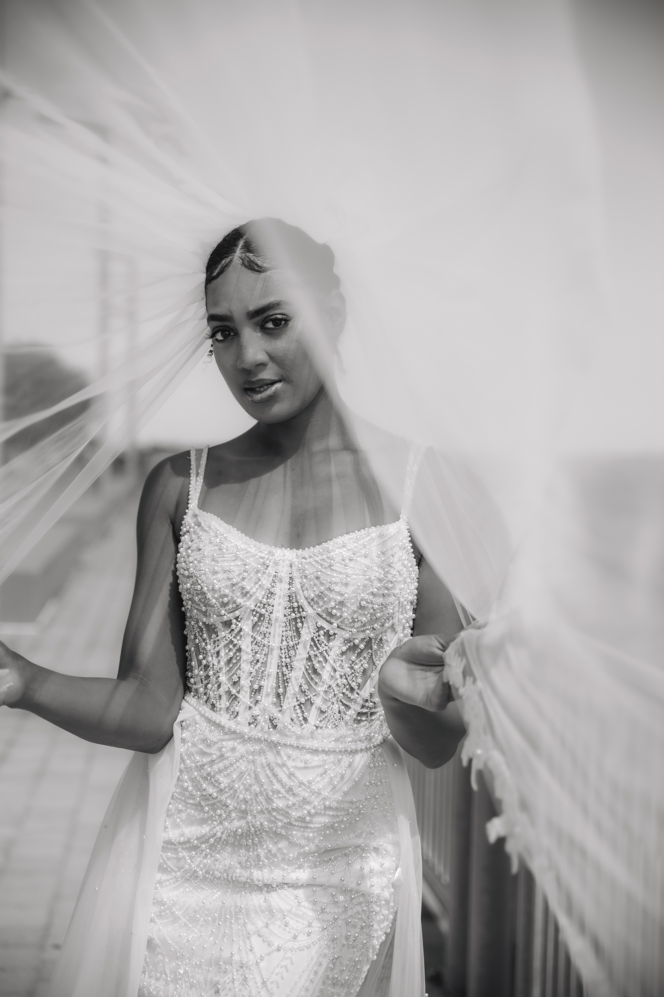 Bride in a detailed wedding gown and veil posing in a black-and-white portrait.