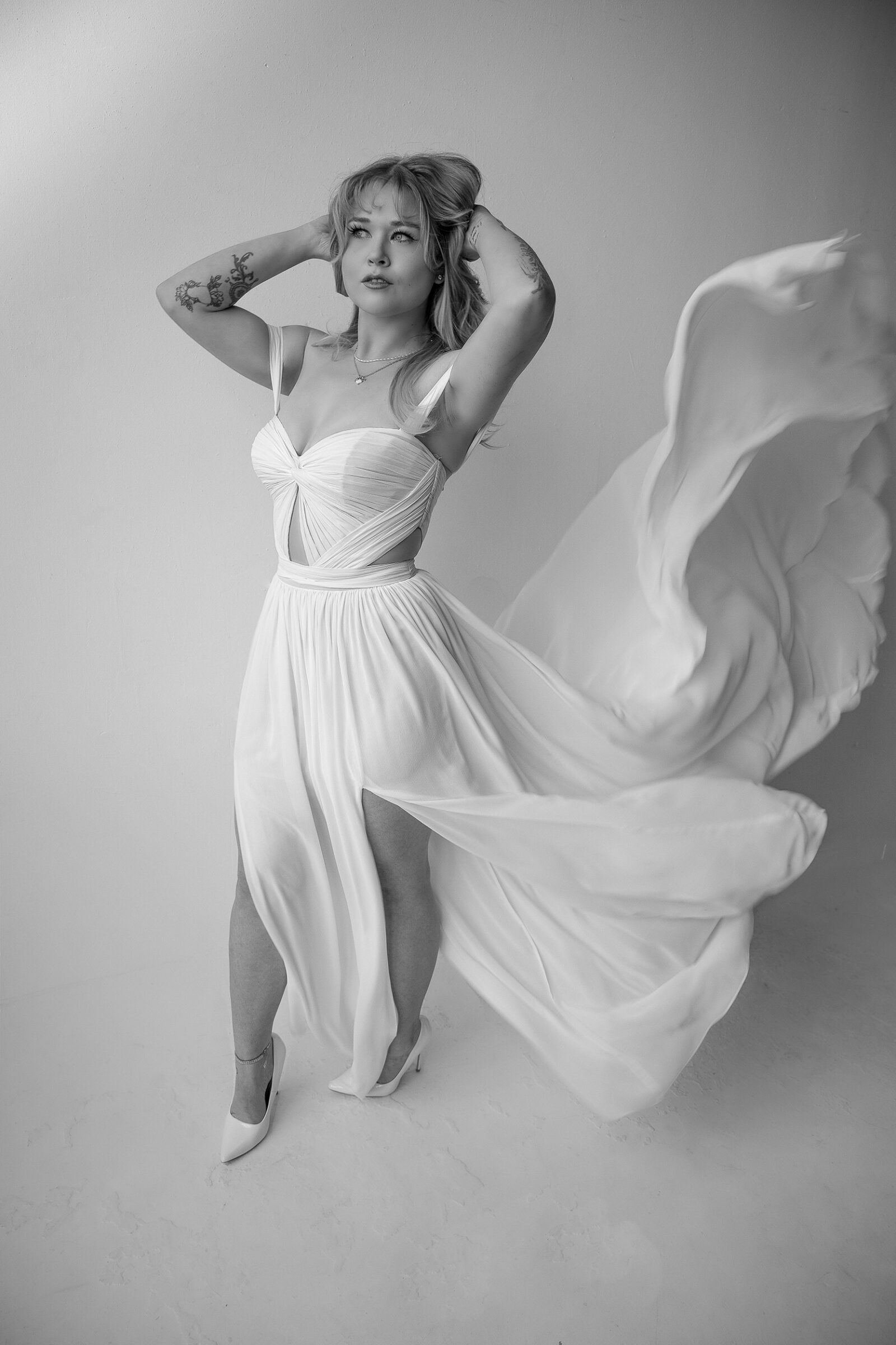 Bride in a flowing white dress posing with a dramatic fabric backdrop in a black-and-white portrait.