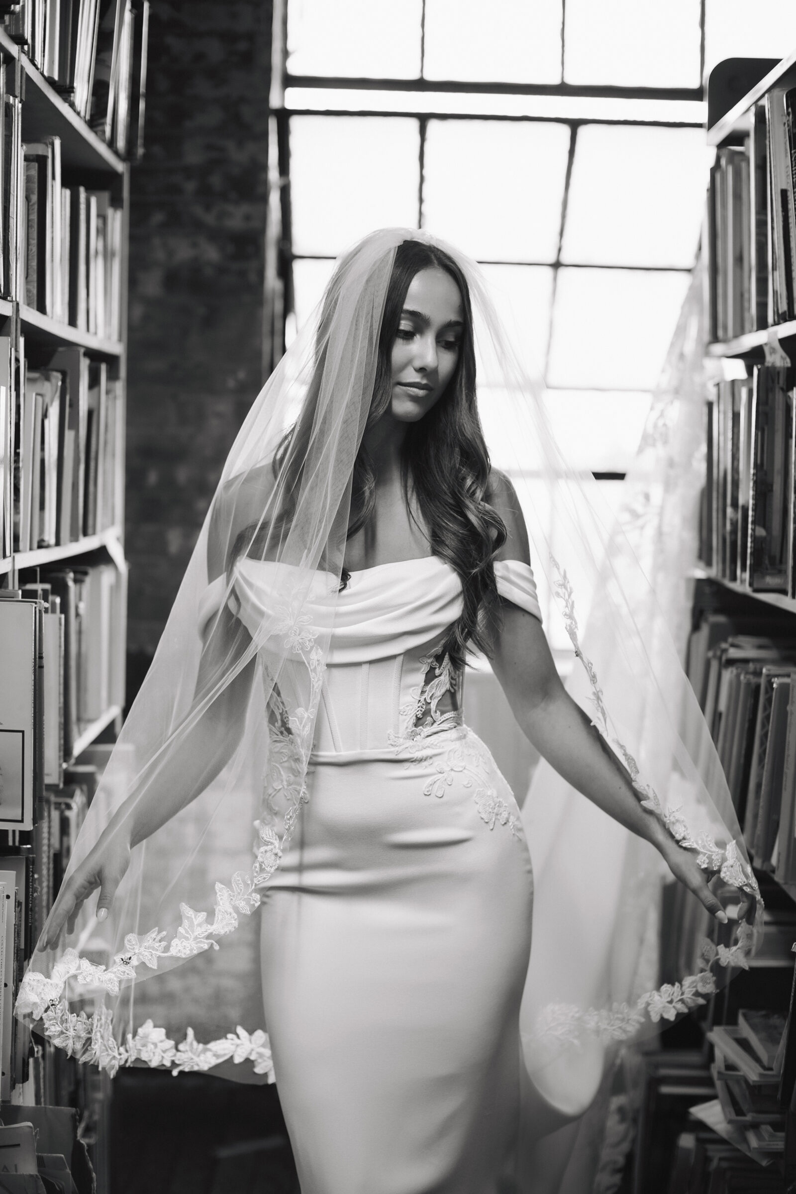 Bride in a fitted wedding dress and veil posing inside a library.