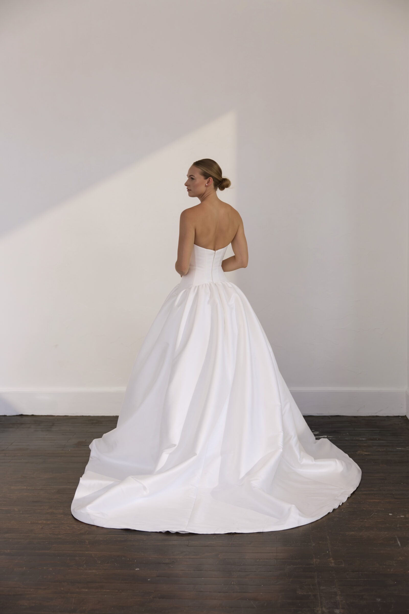 Bride shown from the back wearing a strapless white satin ball gown with a full skirt and long flowing train.