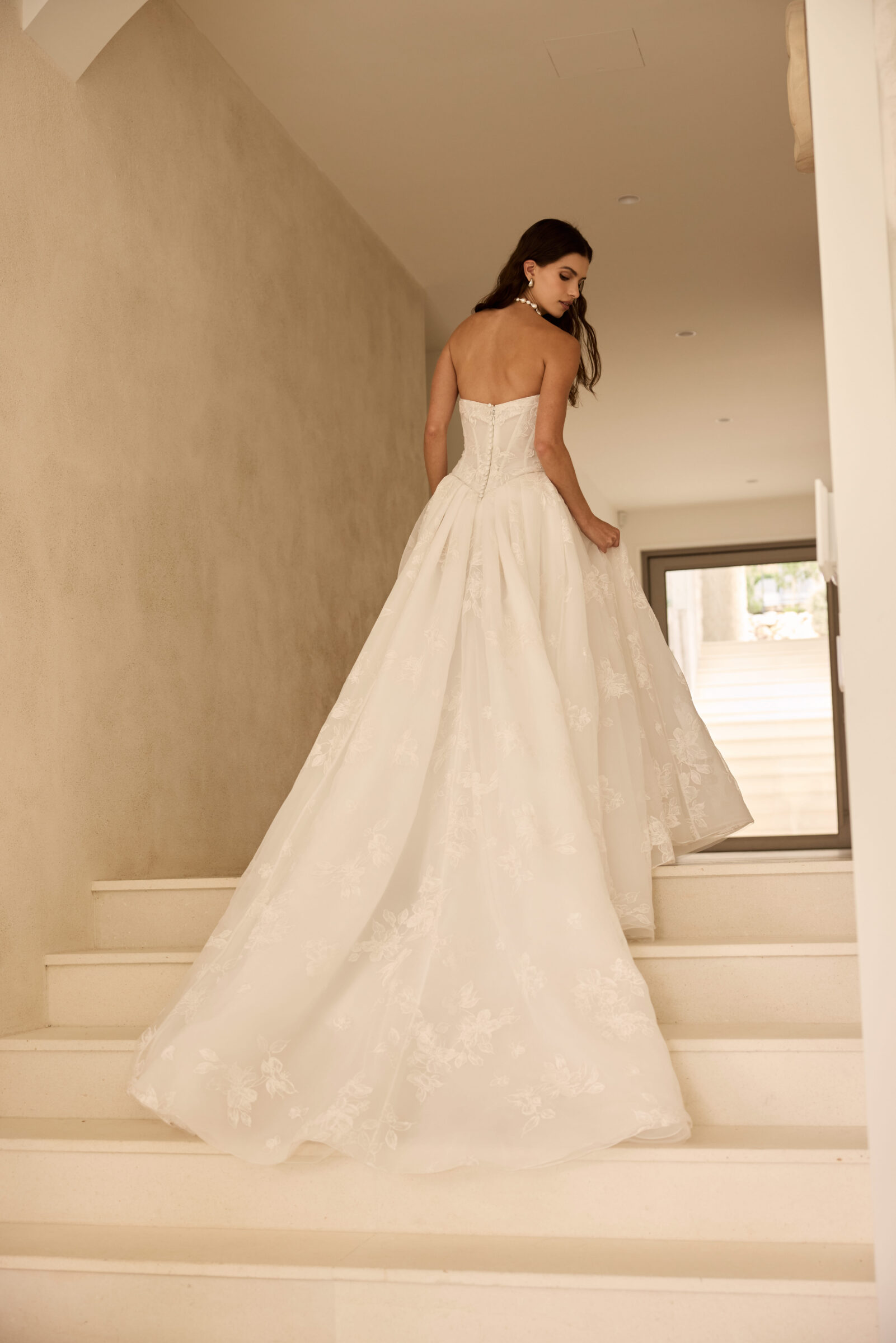 Bride in a strapless white wedding gown with a long flowing train, walking down a staircase.