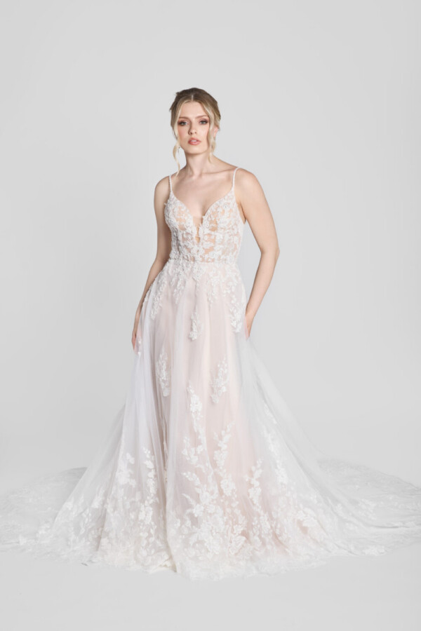 Shy bride wearing a spaghetti strap wedding dress with a deep v cut neckline and floral detailing on the bodice that flows down onto the flowy, tulle skirt.