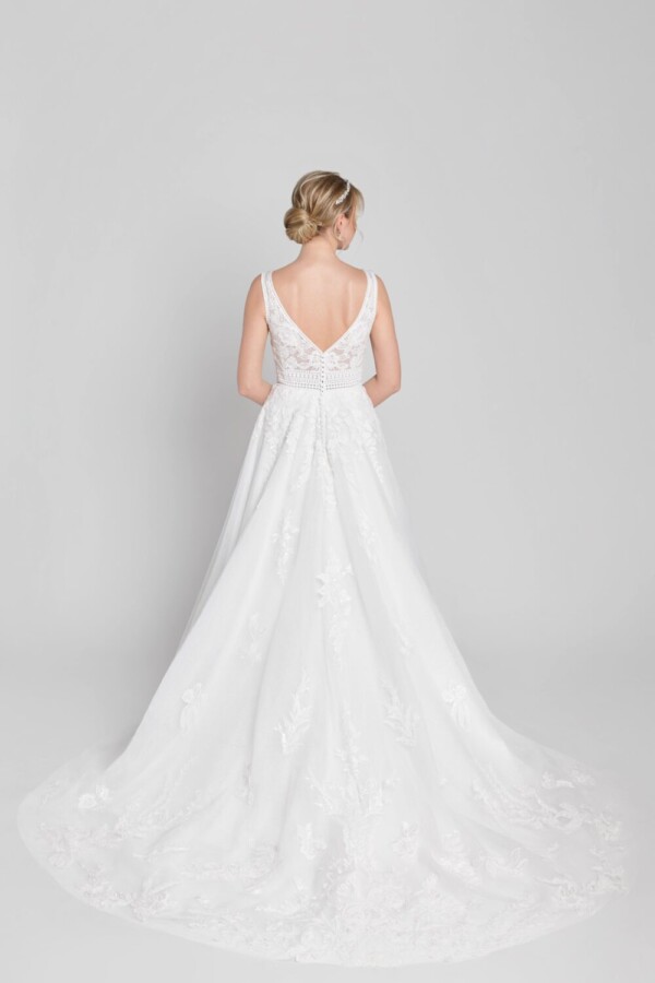 Bride to be looking over her shoulder while wearing her lace wedding dress with a deep back and buttons down the spine. The skirt has lace detailing around the train.