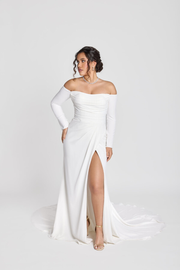 Gorgeous bride wearing a form fitting, off the shoulder, long sleeve wedding dress with a slit in one thigh.