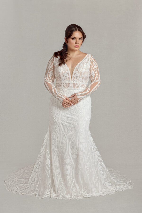 Model wearing the Ashrina, a beacon in modest lace wedding dresses, with her hands folded in front of her.