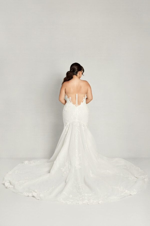 A plus size bride wearing a sweetheart neckline, fit and flare wedding dress with a faux back and sweeping train.