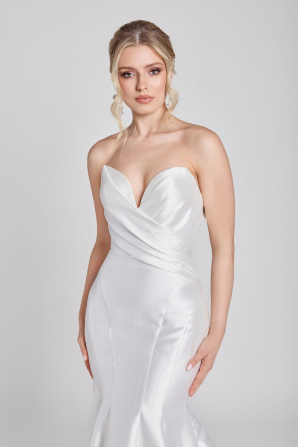 Bride to be wearing a simple fit and flare wedding dress with a deep sweetheart neckline and crossover folding on bodice.