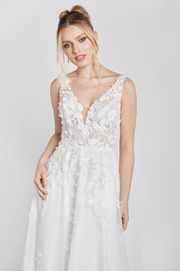 A charming floral wedding gown with lace decals on the bodice that flow onto the skirt worn by a sweet, young bride to be/