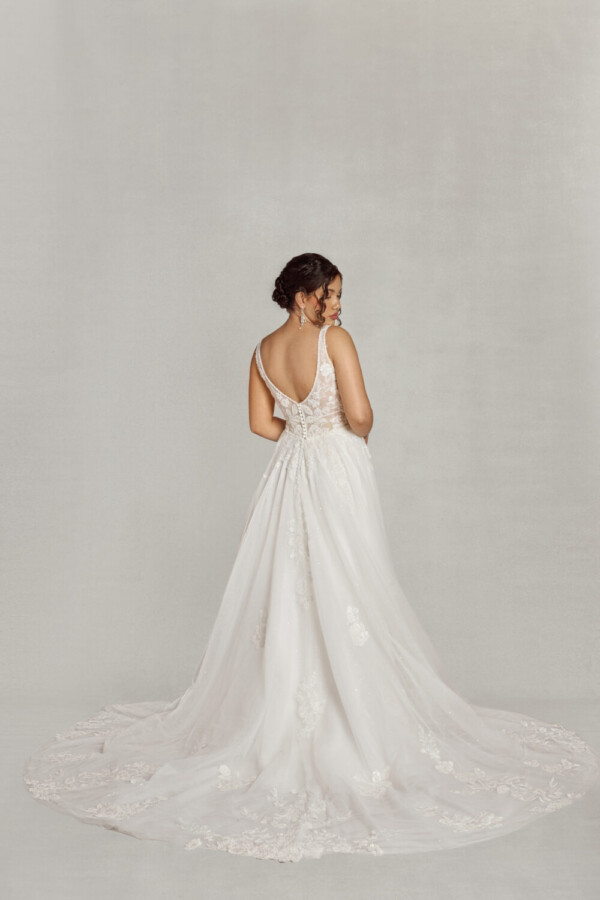 Bride to be wearing a lace wedding dress with a v cut neckline and lace bodice. There are floral decals throughout the different layers of the skirt.