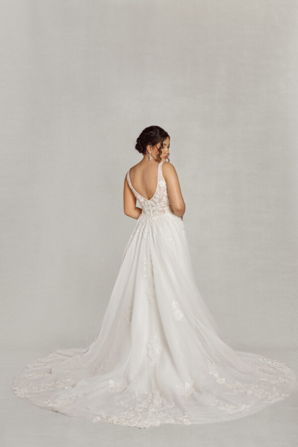 Bride to be wearing a lace wedding dress with a v cut neckline and lace bodice. There are floral decals throughout the different layers of the skirt.