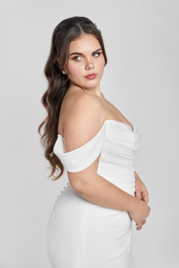 Plus size bride wearing a form fitting wedding dress with off the shoulder sleeves and buttons down the back.