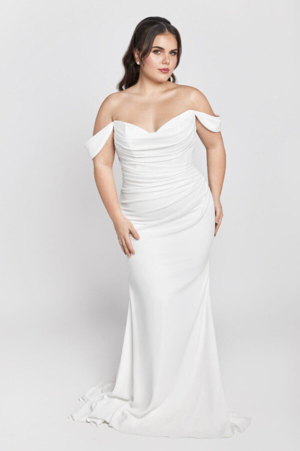 Plus size bride wearing a form fitting wedding dress with off the shoulder sleeves and ruched bodice.