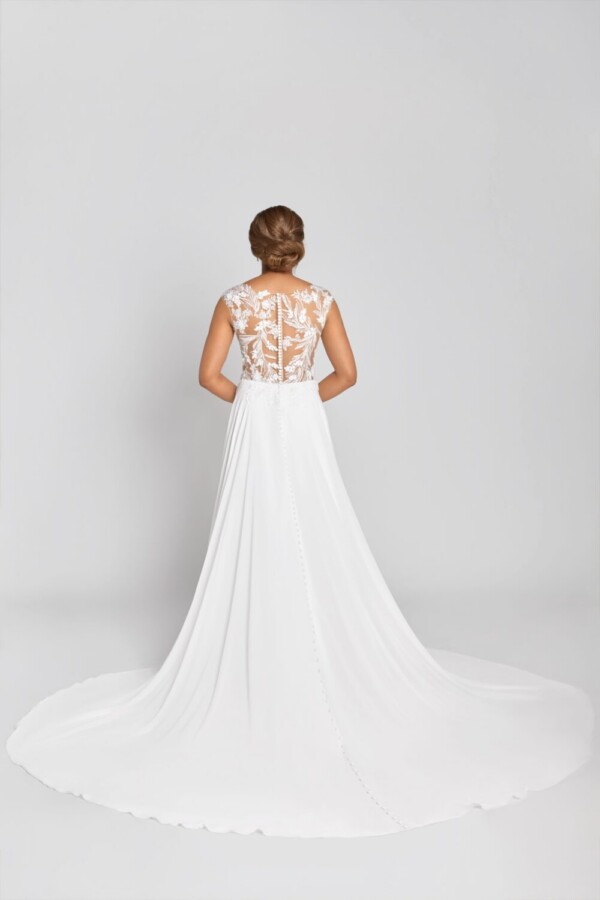 Model wearing a illusion wedding dress with a see through lace back with buttons down the spine and a simple skirt spread around her.