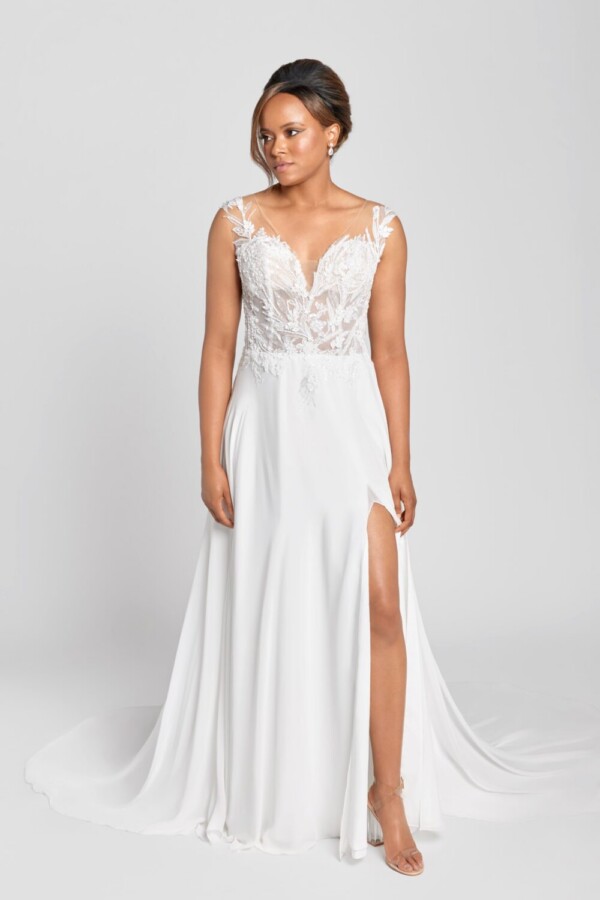 Model wearing a floral lace wedding dress with a see through lace bodice and a simple skirt spread around her and a slit up the thigh.