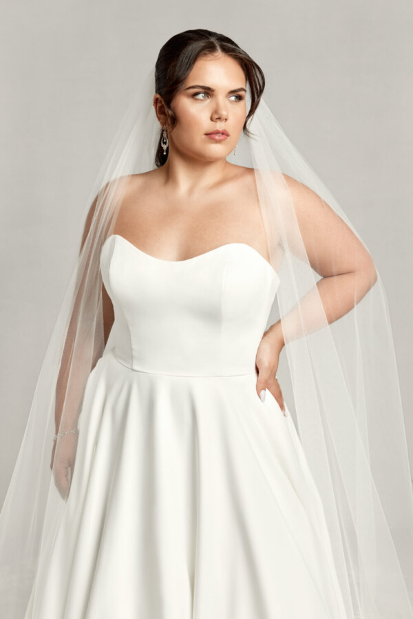 Timeless bride to be wearing a simple wedding dress with a sweetheart neckline and basque waistline. She is also wearing a cathedral length veil.