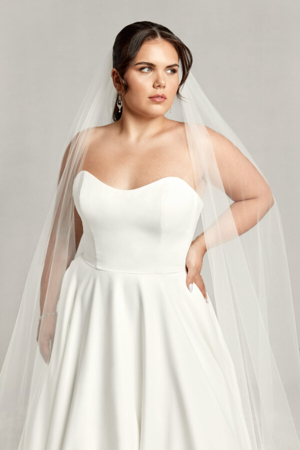Timeless bride to be wearing a simple wedding dress with a sweetheart neckline and basque waistline. She is also wearing a cathedral length veil.
