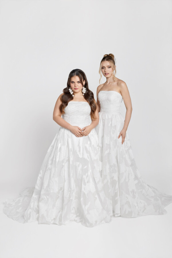 Two brides to be wearing the same strapless wedding dress with patterned fabric on the skirt and a basque waistline.