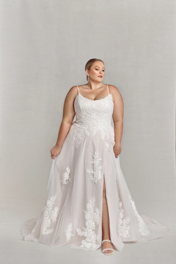 Confident bride to be wearing a blush wedding dress with spaghetti straps and a slit up the thigh.