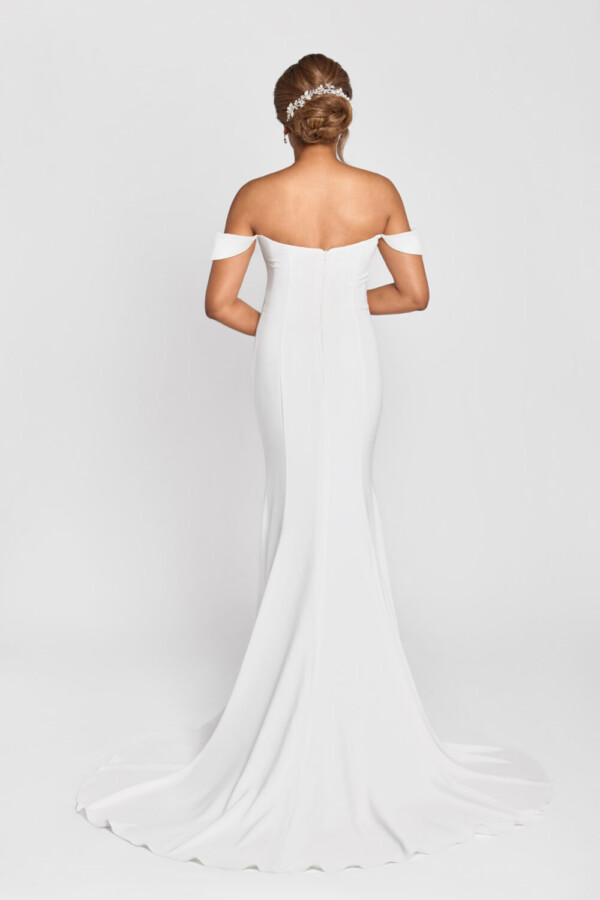 A smiling bride to be wearing an off the shoulder sleeve wedding dress with a ruched bodice and simple skirt.