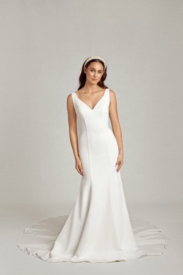 Simple bride to be wearing a traditional, fit and flare wedding dress with a v cut neckline and decorative seams running down the front of the bodice.