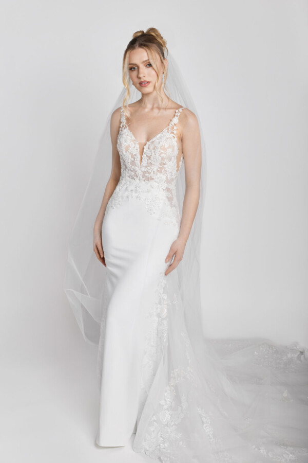 Confident bride to be wearing a wedding dress made of floral lace with spaghetti straps and a star train spread around her.