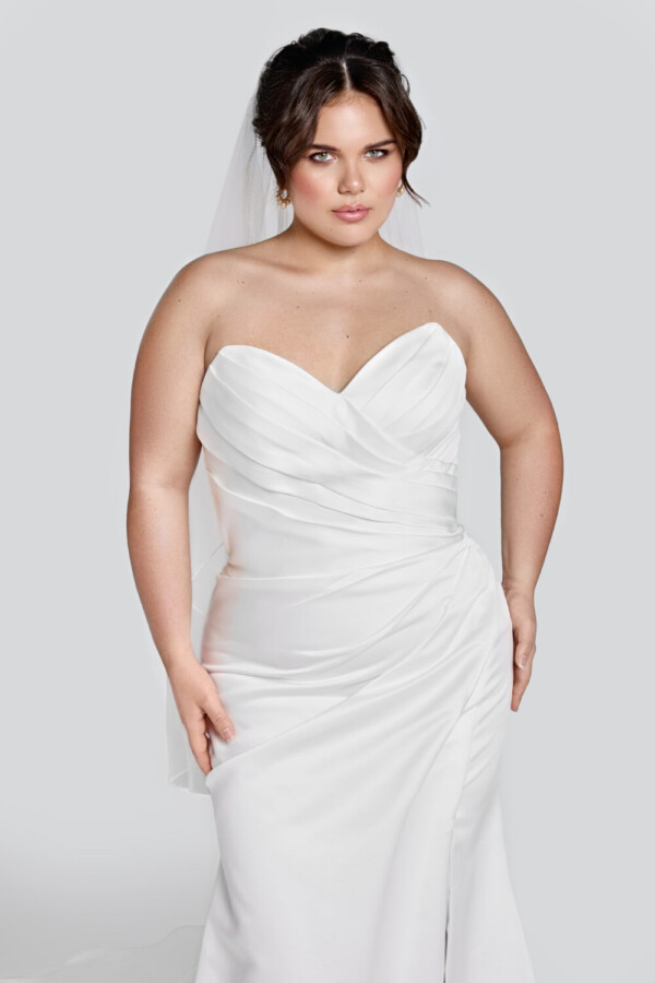 Curvy bride to be wearing a form fitting wedding dress with a sweetheart neckline and fabric gathered at one side.