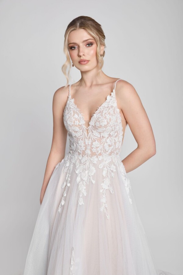 Charming bride to be wearing a spaghetti strap wedding dress with floral lace decals on the bodice and flowing onto the multilayered tulle skirt.