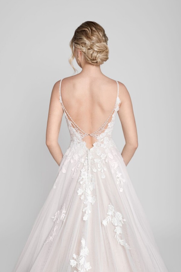 Charming bride to be wearing a spaghetti strap wedding dress with floral lace decals on the deep v back with a small train of buttons.