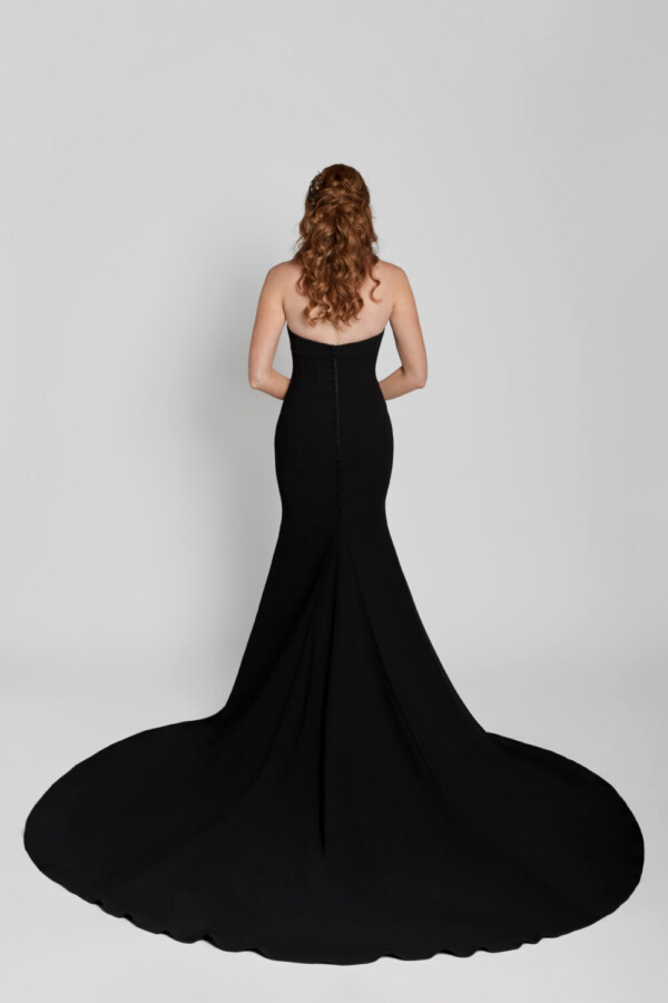 Young bride wearing a black, sheath wedding dress with a sweetheart neckline and corset bodice and the train spread around her.