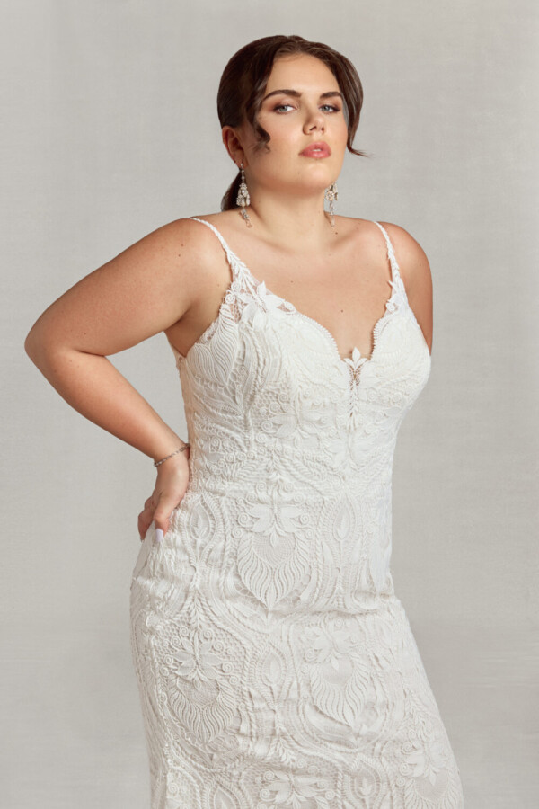An art deco inspired wedding dress with unique lace pattern worn by a bored bride with her hands on her hips.