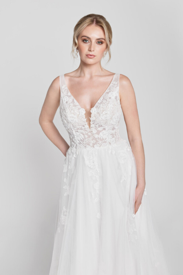 Bride to be wearing a floral lace wedding dress with a deep v cut neckline and multilayered tulle skirt with hidden pockets.