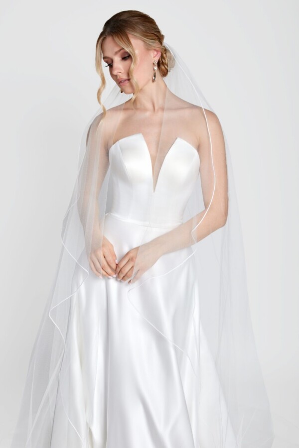 Simple wedding dress with a deep v cut neckline and simple, full skirt worn with a simple, long veil.