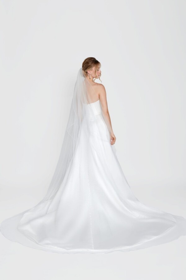 Simple wedding dress with a deep v cut neckline and simple, full skirt worn with a simple, long veil.