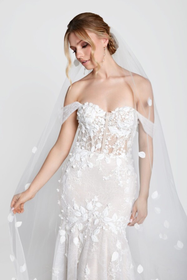 Shy bride to be wearing wedding dress with floral details on the corset bodice flowing onto the fit and flare skirt. She also has a cathedral length veil with leaves embroidered on it.