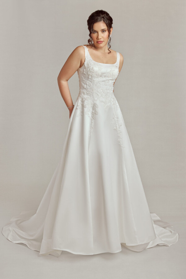 Bride to be wearing a wedding dress with scoop neckline and floral details flowing from the bodice onto the full skirt with a simple train.