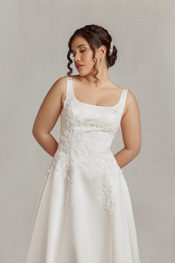 Bride to be wearing a wedding dress with scoop neckline and floral details flowing from the bodice onto the full skirt.
