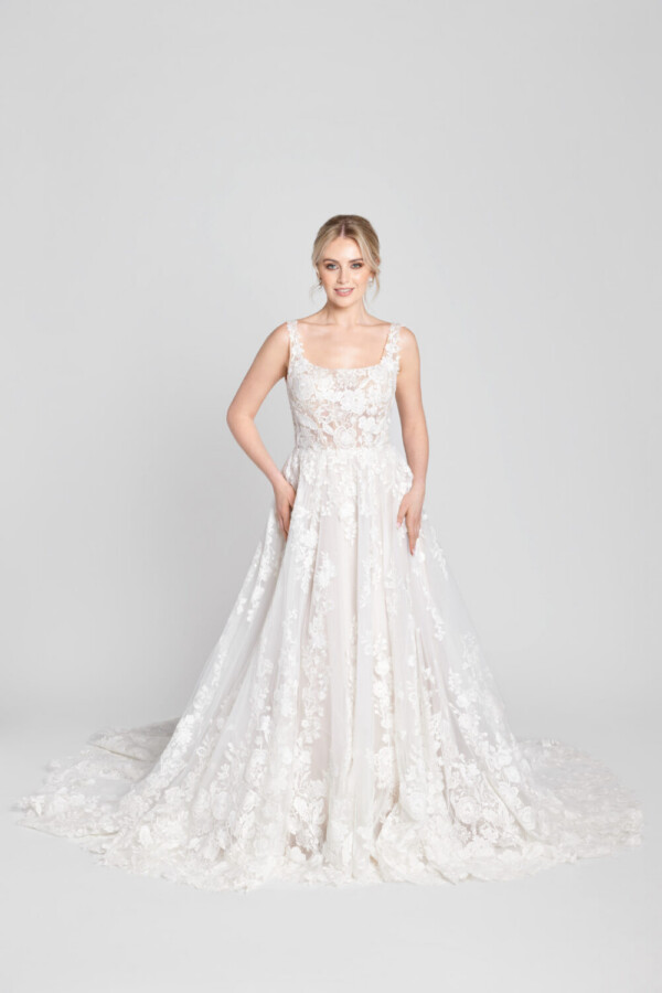 Sweet bride to be wearing a scoop neck wedding dress with floral detailing on the bodice flowing onto the multilayered skirt and lace train.