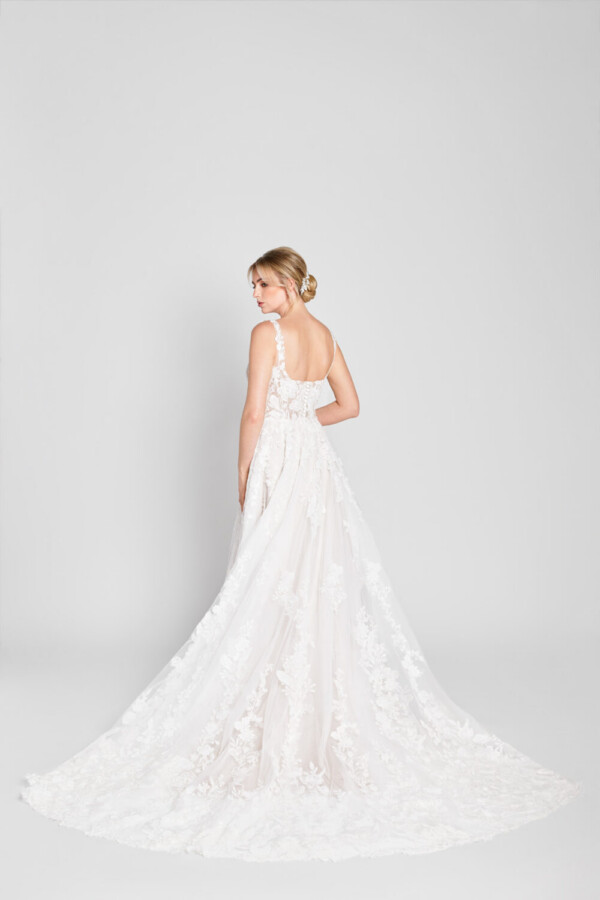 Sweet bride to be wearing a scoop neck wedding dress with floral detailing on the bodice flowing onto the multilayered skirt and lace train.