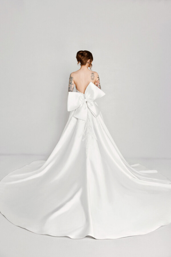 A bride with tattoos in a white fitted slim strap dress with a bow on the back.