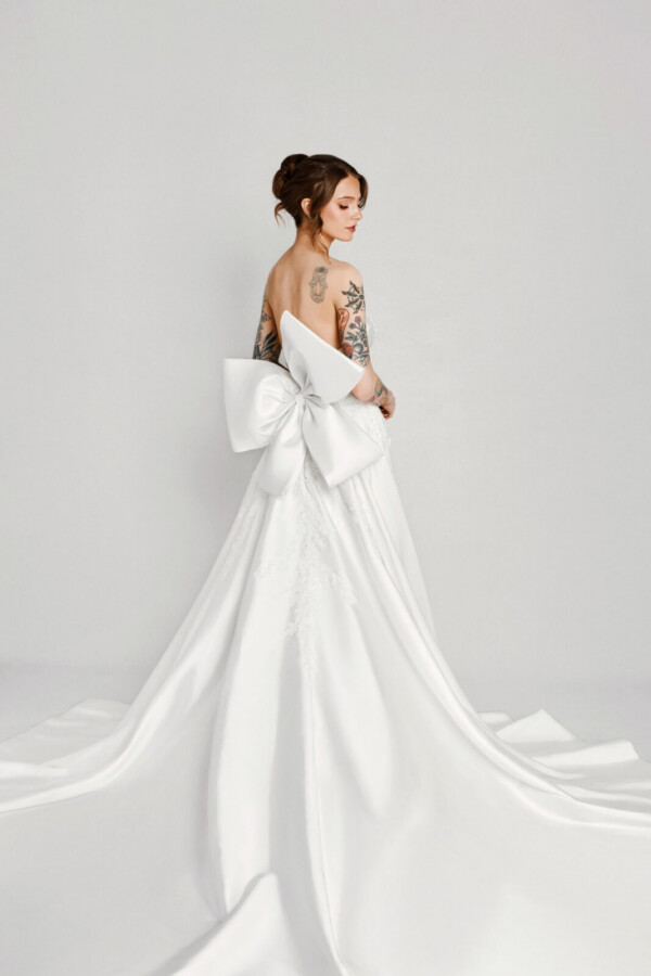 A bride with tattoos in a white fitted slim strap dress with a bow on the back.